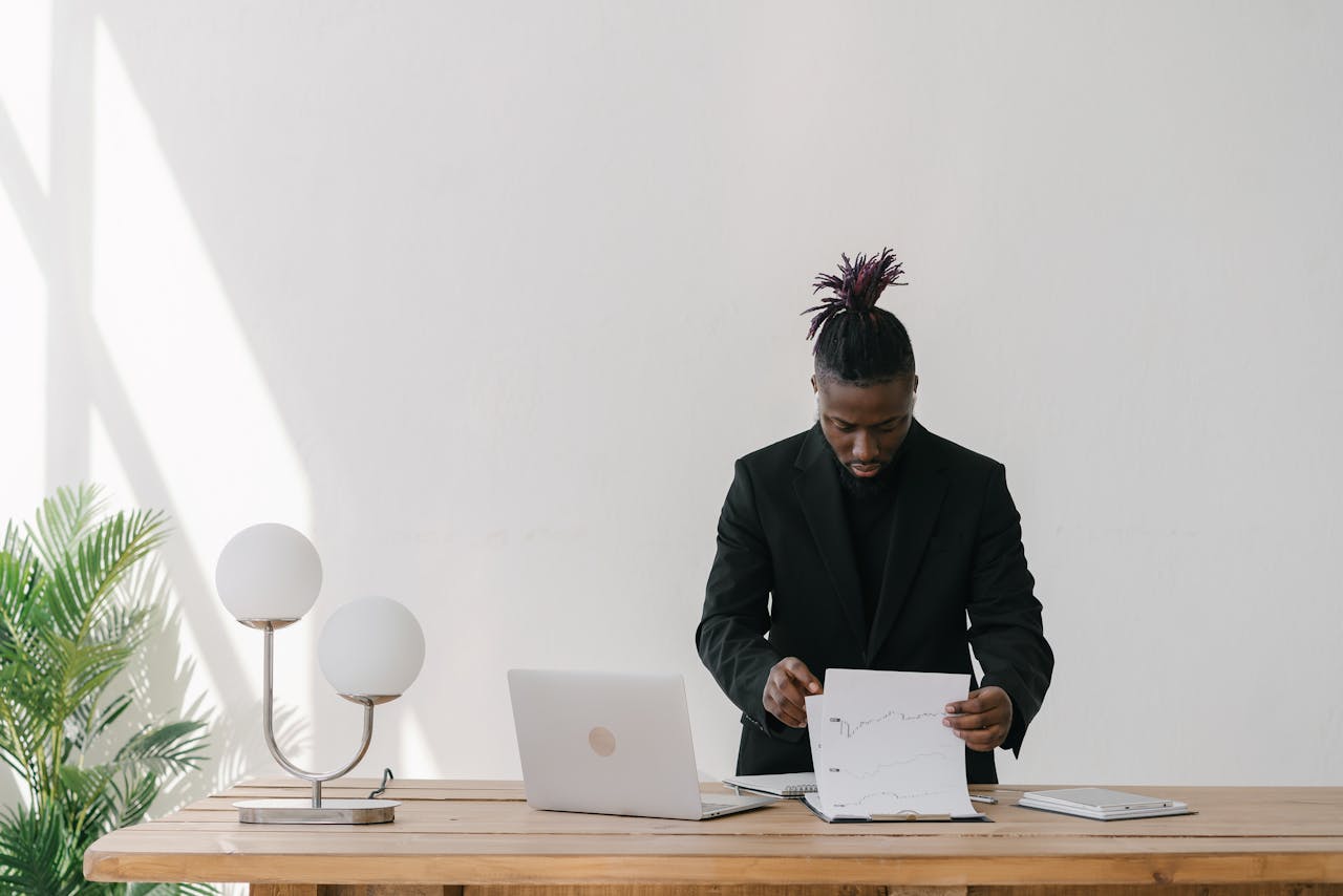 A focused businessman analyzing charts in a bright office with a laptop and papers.