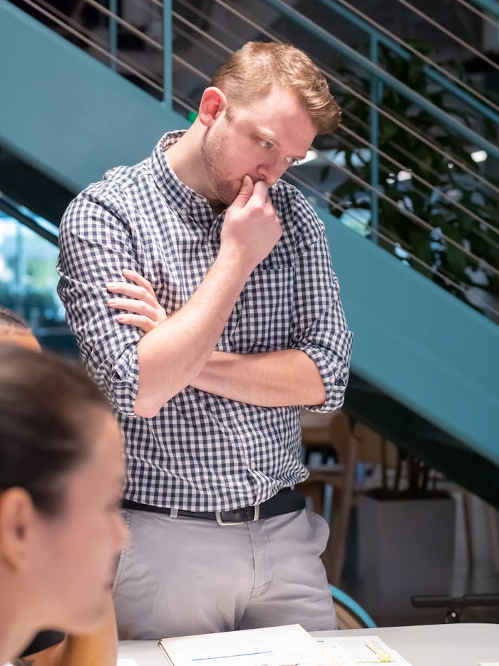 Man in a plaid shirt deep in thought while working in a modern office.
